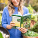 Smiling woman reads "The 5-Minute Gardener" book by Nicole Johnsey Burke, with fresh garlic and kale harvest.