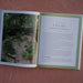 Open gardening book. Left: kitchen garden photo with raised beds, person. Right: "Install the Kitchen Garden Structures" text.