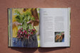 Open cookbook. Left: Hands hold a large bunch of freshly harvested radishes with green tops & soil. Right: "Roots" text & carrots.
