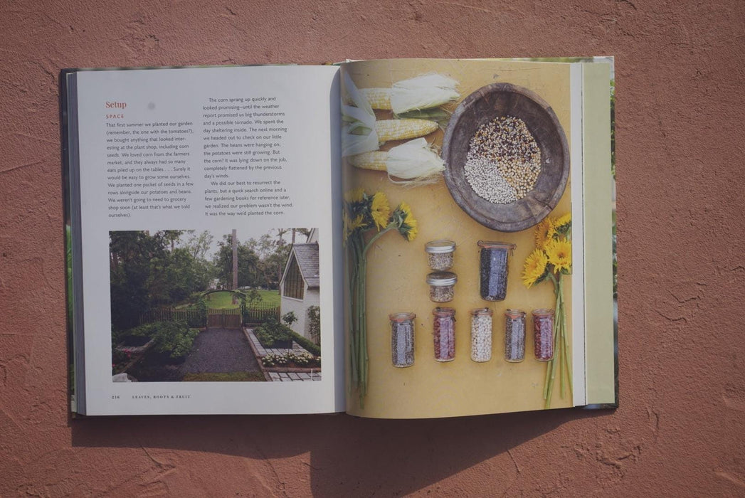 Cookbook spread featuring harvested corn, dried beans, seeds, preserved grains in jars, yellow flowers, and a home garden.