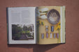 Cookbook spread featuring harvested corn, dried beans, seeds, preserved grains in jars, yellow flowers, and a home garden.