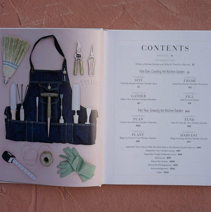 Kitchen garden book open to contents page and gardening tools: denim apron, trowel, shears, gloves, broom, measuring tape.