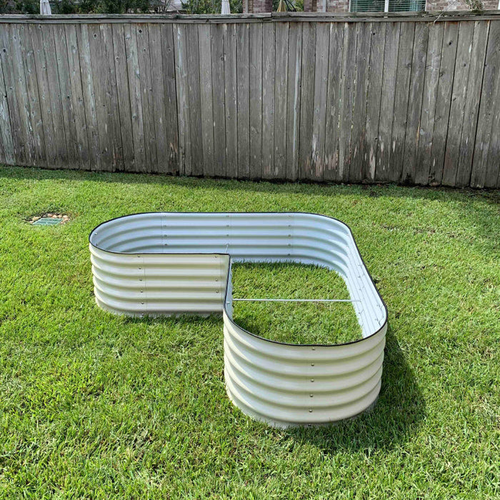 L-shaped galvanized steel raised garden bed on green grass. Durable corrugated metal planter for backyard gardening.