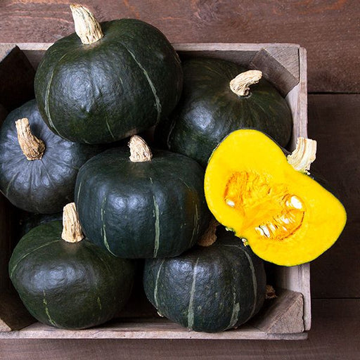 Dark green Kabocha winter squash in a wooden crate, one sliced revealing vibrant yellow flesh and seeds. Fresh harvest.