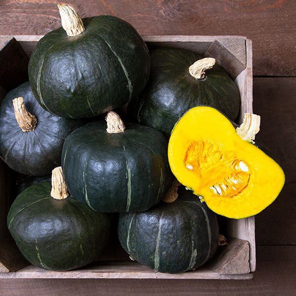 Dark green Kabocha winter squash in a wooden crate, one sliced revealing vibrant yellow flesh and seeds. Fresh harvest.