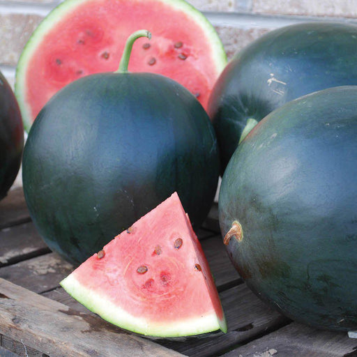 Dark green watermelons: whole, half, and a slice showing sweet red flesh with seeds on a wooden table.