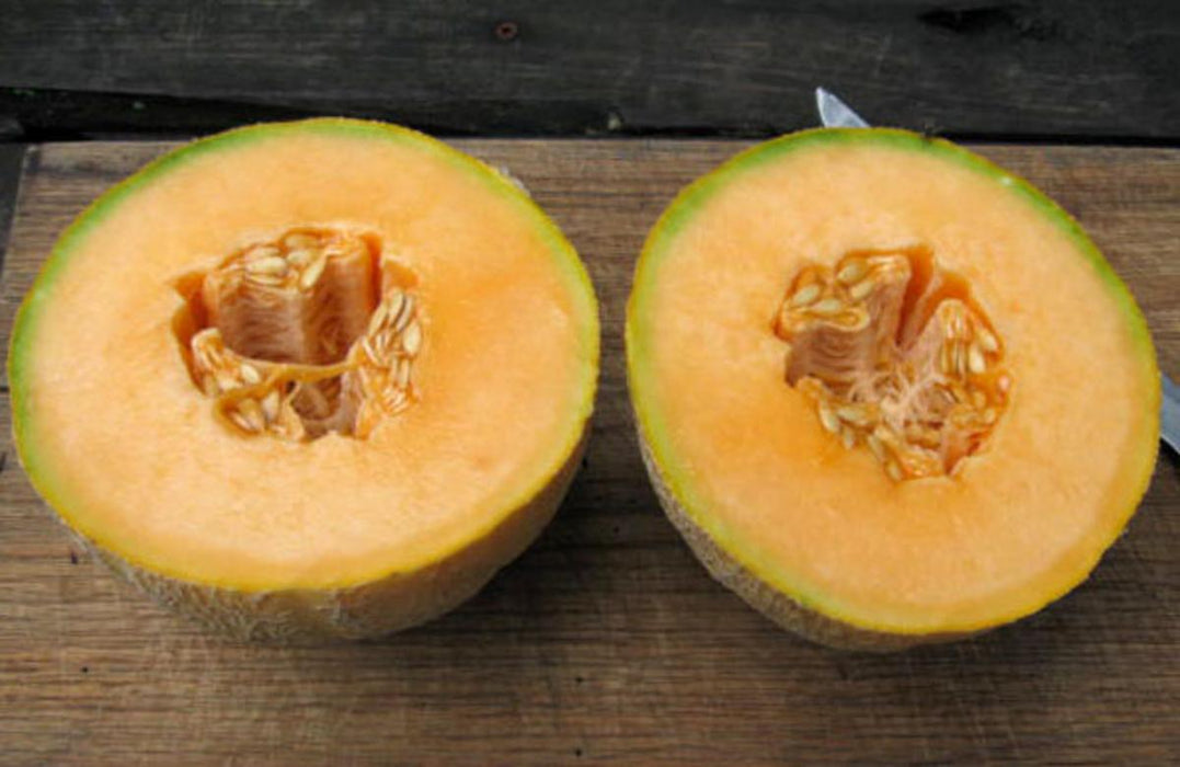 Ripe cantaloupe melon halves with bright orange flesh and seeds on a wooden cutting board.