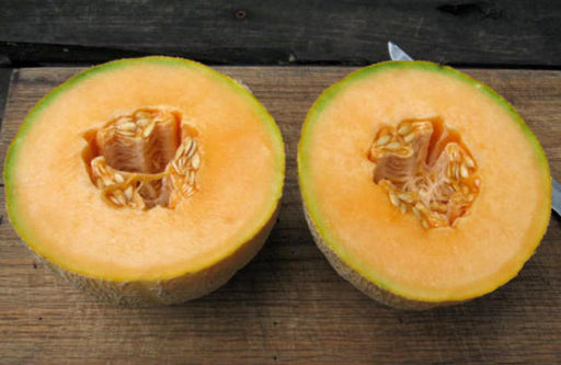 Ripe cantaloupe melon halves with bright orange flesh and seeds on a wooden cutting board.