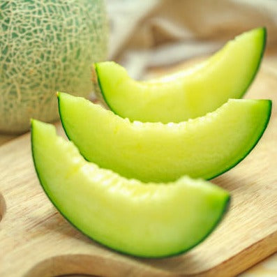Fresh green melon slices on wooden cutting board with whole netted melon. Sweet, healthy fruit.
