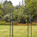 Black metal garden arch with decorative top and lattice trellis in a grassy yard.