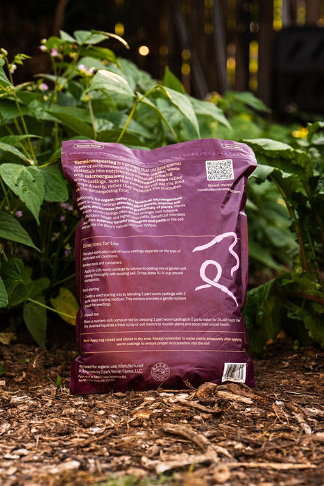 Purple bag of organic vermicompost worm castings for healthy garden plants, sitting on mulch.