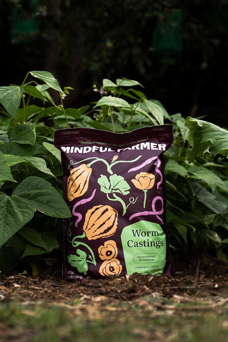 Mindful Farmer Worm Castings soil amendment bag with gourd and worm designs, in a green garden.