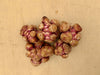 Knobby Jerusalem artichokes with reddish-purple skin on a light wood surface. Fresh sunchoke tubers, root vegetable.