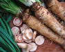 Fresh horseradish roots, green leaves, and sliced pieces displaying white and pink interiors on a wooden surface.