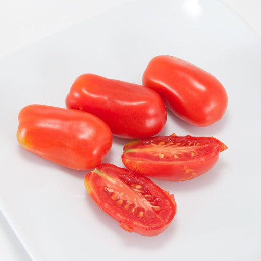 Fresh red Roma tomatoes on a white surface. Three whole and two halved, revealing seeds. Healthy cooking ingredient.