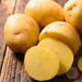 Fresh golden potatoes, whole and sliced, on a rustic wooden table. Raw produce for cooking and healthy meals.