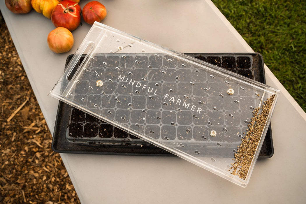 Mindful Farmer seed sower on a soil-filled propagation tray with tiny seeds. Fresh heirloom tomatoes await planting.
