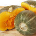 Green striped winter squash, one whole and two halves, displaying vibrant orange flesh on a wooden board.