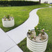 White corrugated metal raised garden beds flank a winding concrete path through a lush green lawn, leading to a lake.
