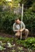 Gardener inspecting young vegetable leaves with a hoe in a thriving garden. Sustainable growing, fresh produce.