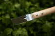 Gardening weeder with a serrated metal blade and natural wood handle, ideal for effective weed removal and cultivation.