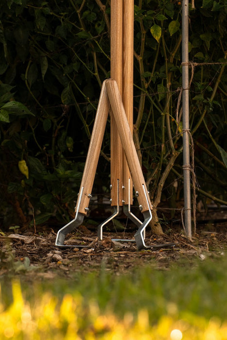 Three premium garden hoes with wooden handles and steel blades stand in rich soil, surrounded by lush green plants.