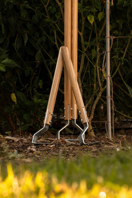 Three premium garden hoes with wooden handles and steel blades stand in rich soil, surrounded by lush green plants.