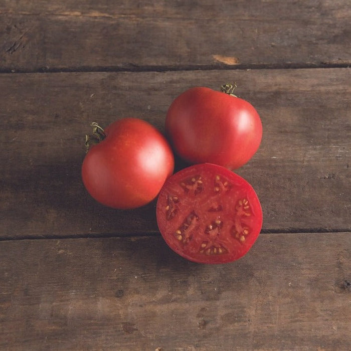 Fresh red tomatoes, two whole and one sliced, on a rustic wooden table. Ripe garden produce.