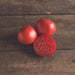 Fresh red tomatoes, two whole and one sliced, on a rustic wooden table. Ripe garden produce.
