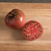 Whole & sliced red-purple heirloom tomato on wood. Vibrant red flesh, seeds, green stem visible.