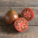 Dark heirloom tomato, whole and sliced, showing red flesh and green seed chambers on rustic wood.