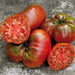 Ripe heirloom tomatoes, some sliced, showing deep red flesh, green shoulders, and seeds on a stone background.