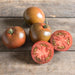 Whole and sliced dark heirloom tomatoes on rustic wood. Fresh garden produce.