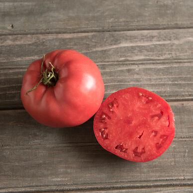 Whole and sliced pink heirloom tomato on a rustic wooden table. Fresh, ripe produce for cooking and salads.
