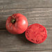 Whole and sliced pink heirloom tomato on a rustic wooden table. Fresh, ripe produce for cooking and salads.