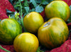 Vibrant Green Zebra heirloom tomatoes, yellow with green stripes, resting on a red patterned cloth with vine leaves.