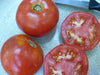 Fresh, ripe red tomatoes: two whole, two sliced open on a patterned surface with a knife. Healthy produce for cooking.