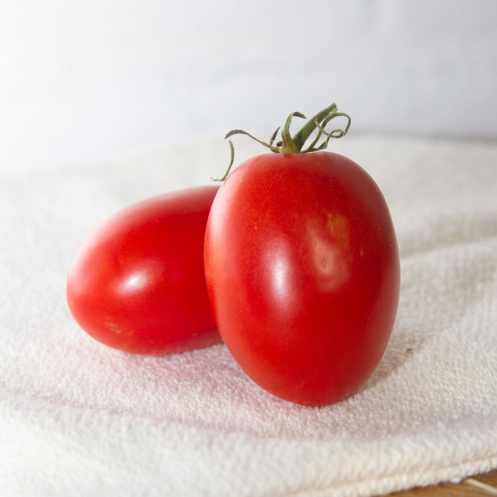Two ripe red Roma tomatoes with green stems on a white towel. Fresh produce.