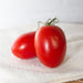 Two ripe red Roma tomatoes with green stems on a white towel. Fresh produce.