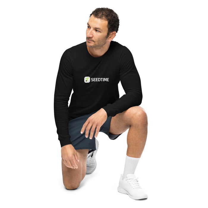 Man kneeling in black Seedtime long-sleeve shirt, dark shorts, and white sneakers. Casual athletic wear.