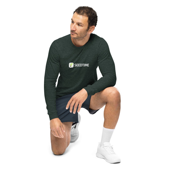 Dark green long-sleeve SEEDTIME t-shirt worn by a man in dark shorts and white sneakers, kneeling.