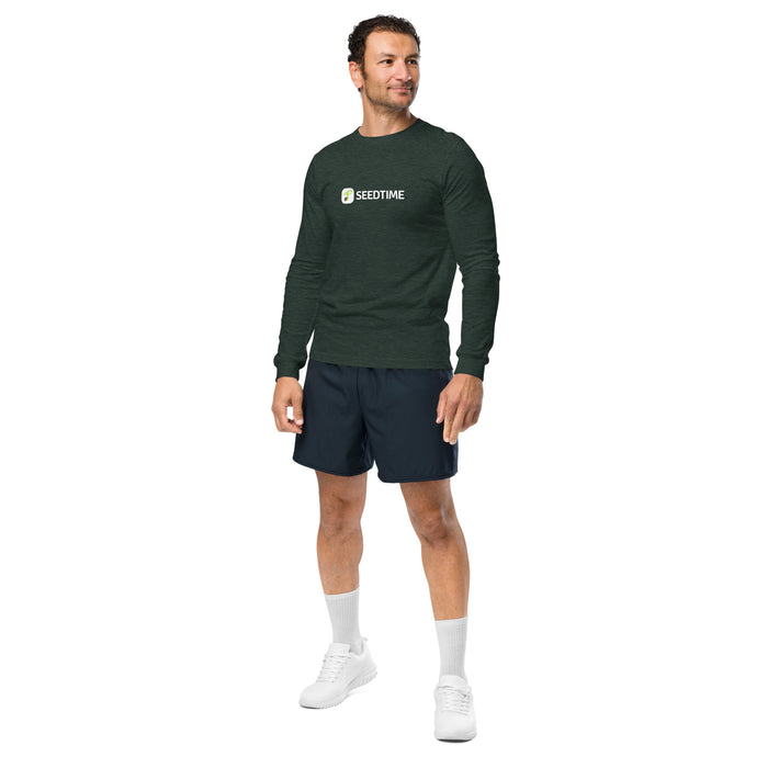 Male model in dark green Seedtime long-sleeve shirt. Comfortable men's athletic wear, navy shorts, white sneakers.