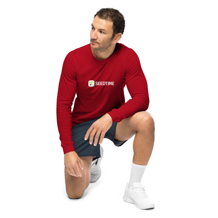 Man wearing red long-sleeve Seedtime logo shirt, athletic shorts, and white sneakers, kneeling.