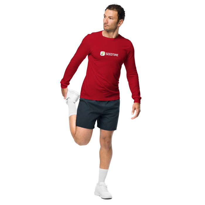 Man in red Seedtime long-sleeve shirt, navy shorts, stretching leg. Men's activewear, workout clothes.