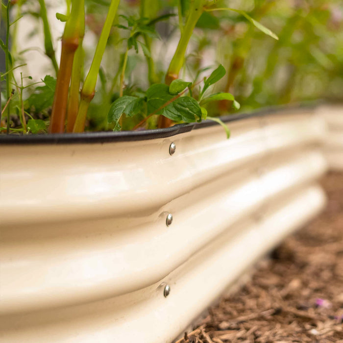 Corrugated beige raised garden bed with lush green plants, black trim, and garden mulch.