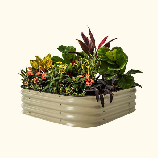 Tan corrugated metal raised garden bed with diverse, vibrant plants, colorful foliage, and orange, yellow flowers. Outdoor planter.