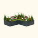L-shaped dark gray raised garden bed with a vibrant mix of green foliage, orange, pink, and white flowers.