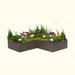 L-shaped dark grey planter box with vibrant flowers, evergreen shrubs, and tall grasses for modern outdoor landscaping.
