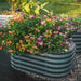 Vibrant pink and orange lantana flowers in a dark green corrugated metal raised garden bed with wood chip mulch.