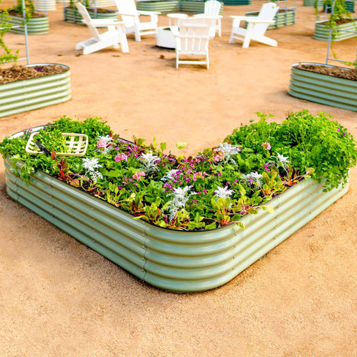 Sage V-shaped corrugated raised garden bed filled with herbs, vegetables, and flowers. Outdoor patio with white Adirondack chairs.